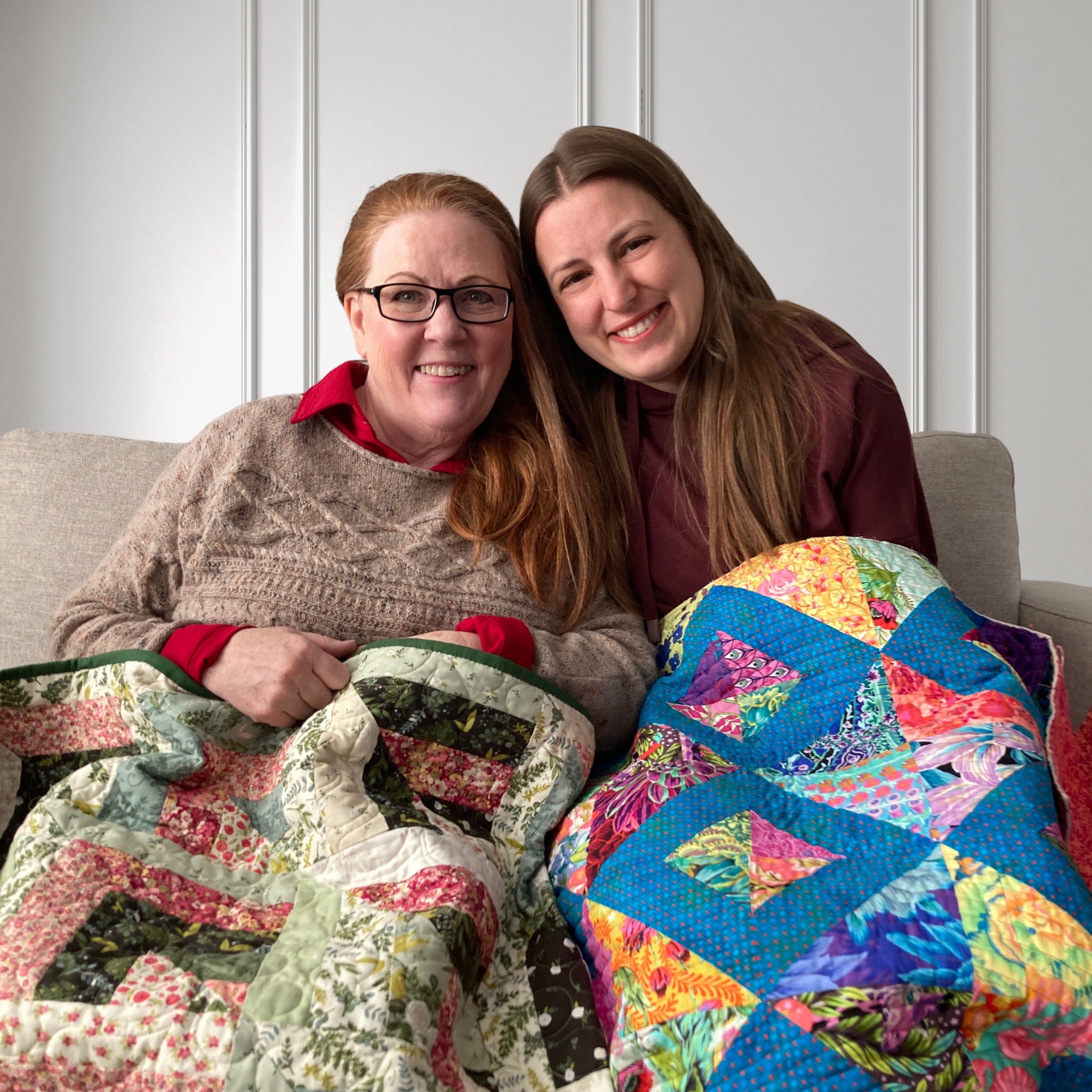 Cheryl and Marsali sitting together, each holding a quilt they made for the other